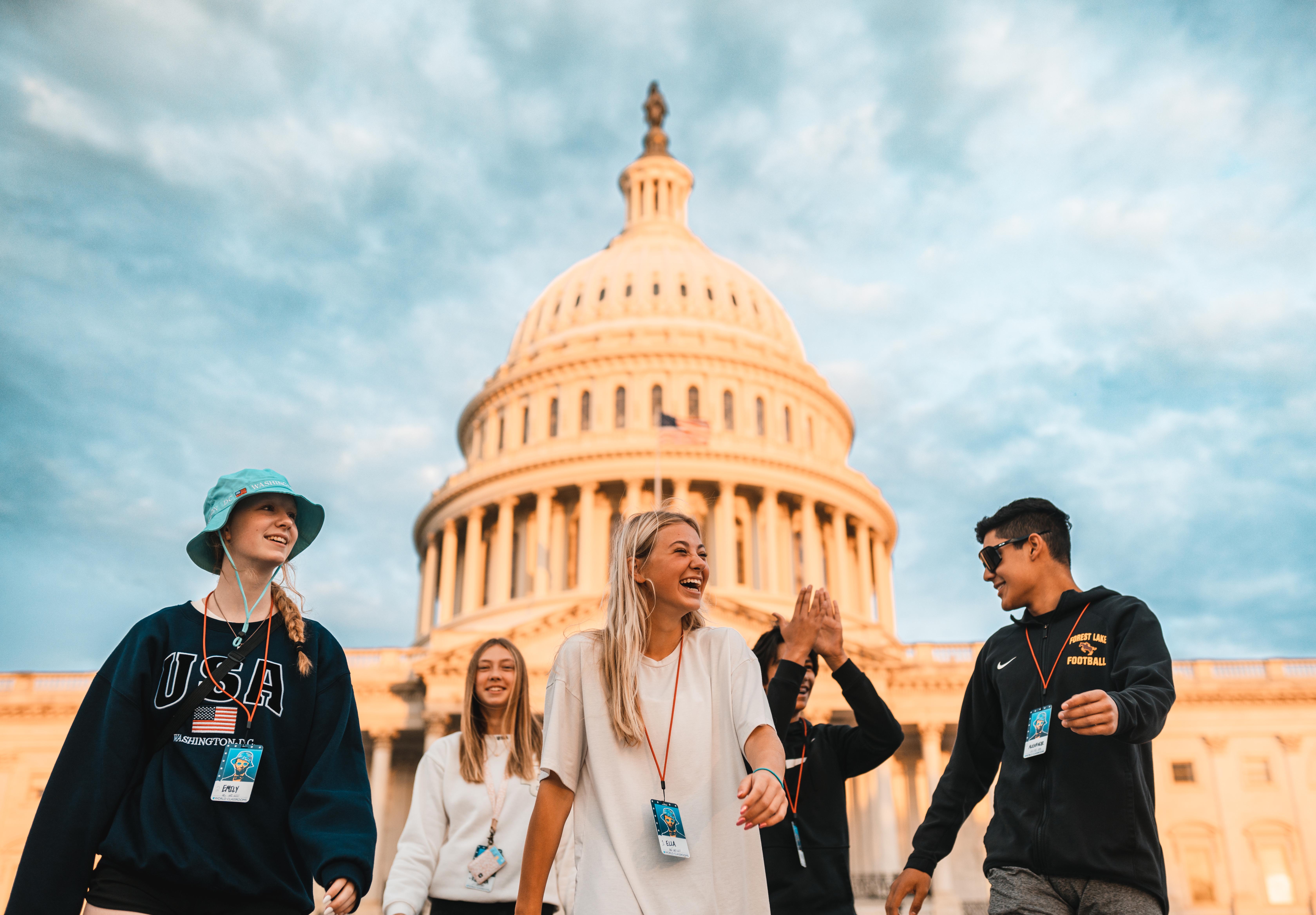 A group of high school students laugh and high-five together in front of the U.S. Capitol building.