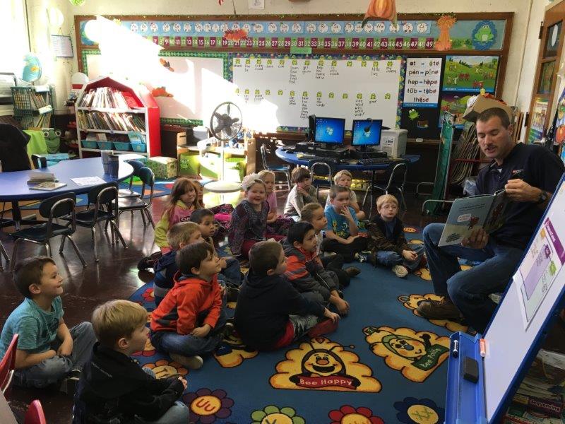 Teacher reads a book to children sitting on a colorful rug in a classroom.