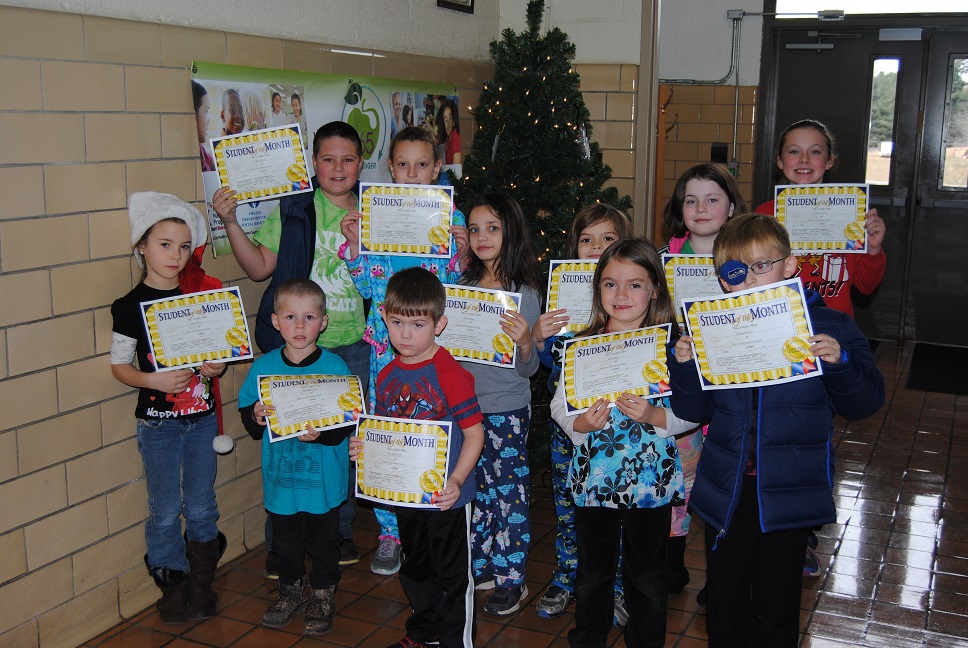Students in a hallway hold "Student of the Month" certificates near a Christmas tree.