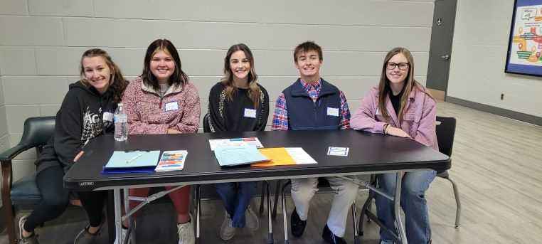 Students sitting at a table ready to greet the public