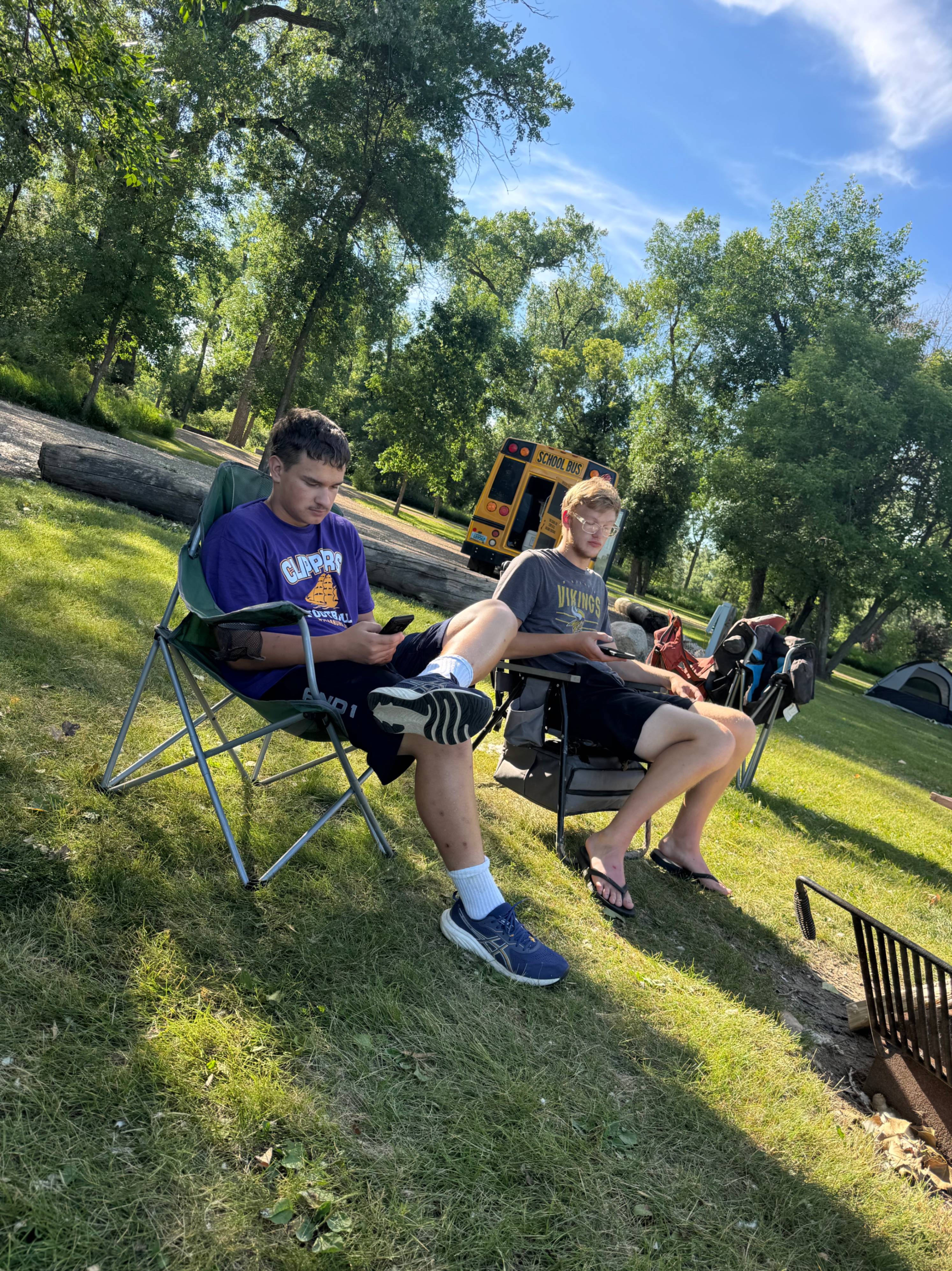 two students sitting in camping chairs on phones