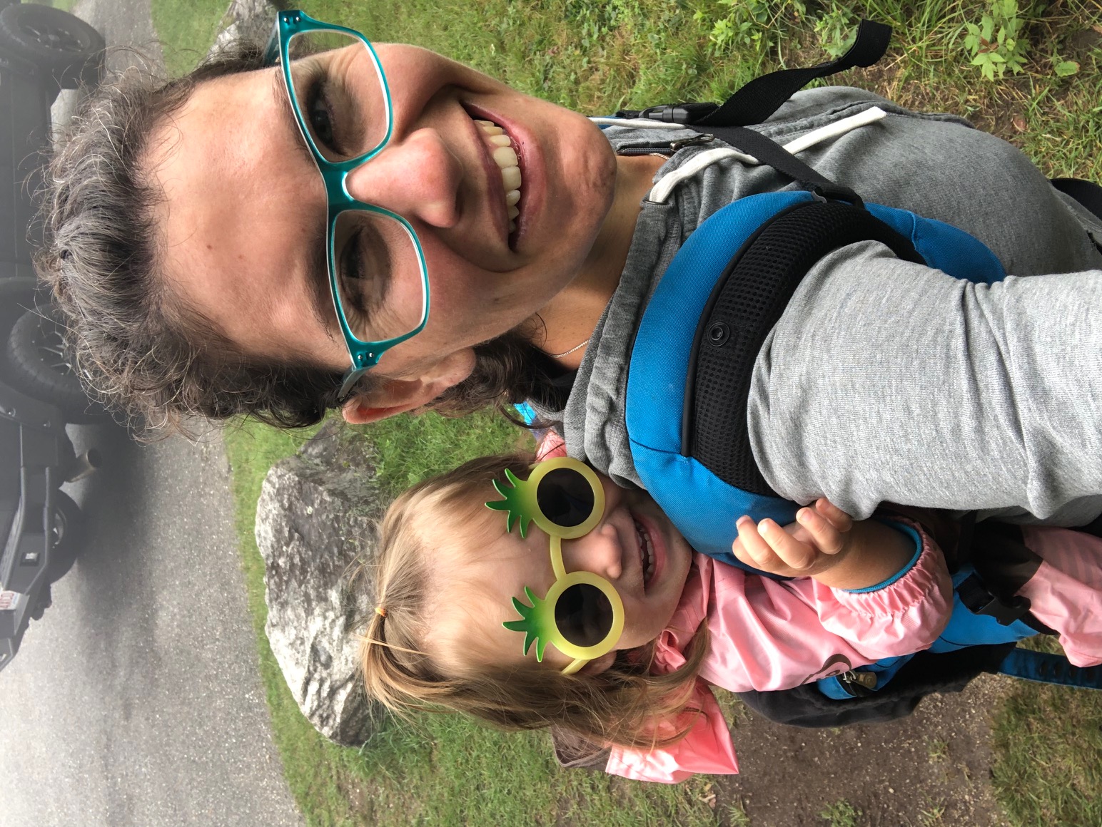 Selfie of a white woman with glasses and her hair back holding a child with pineapple shaped glasses on her back. Jocelyn York Guidance Counselor