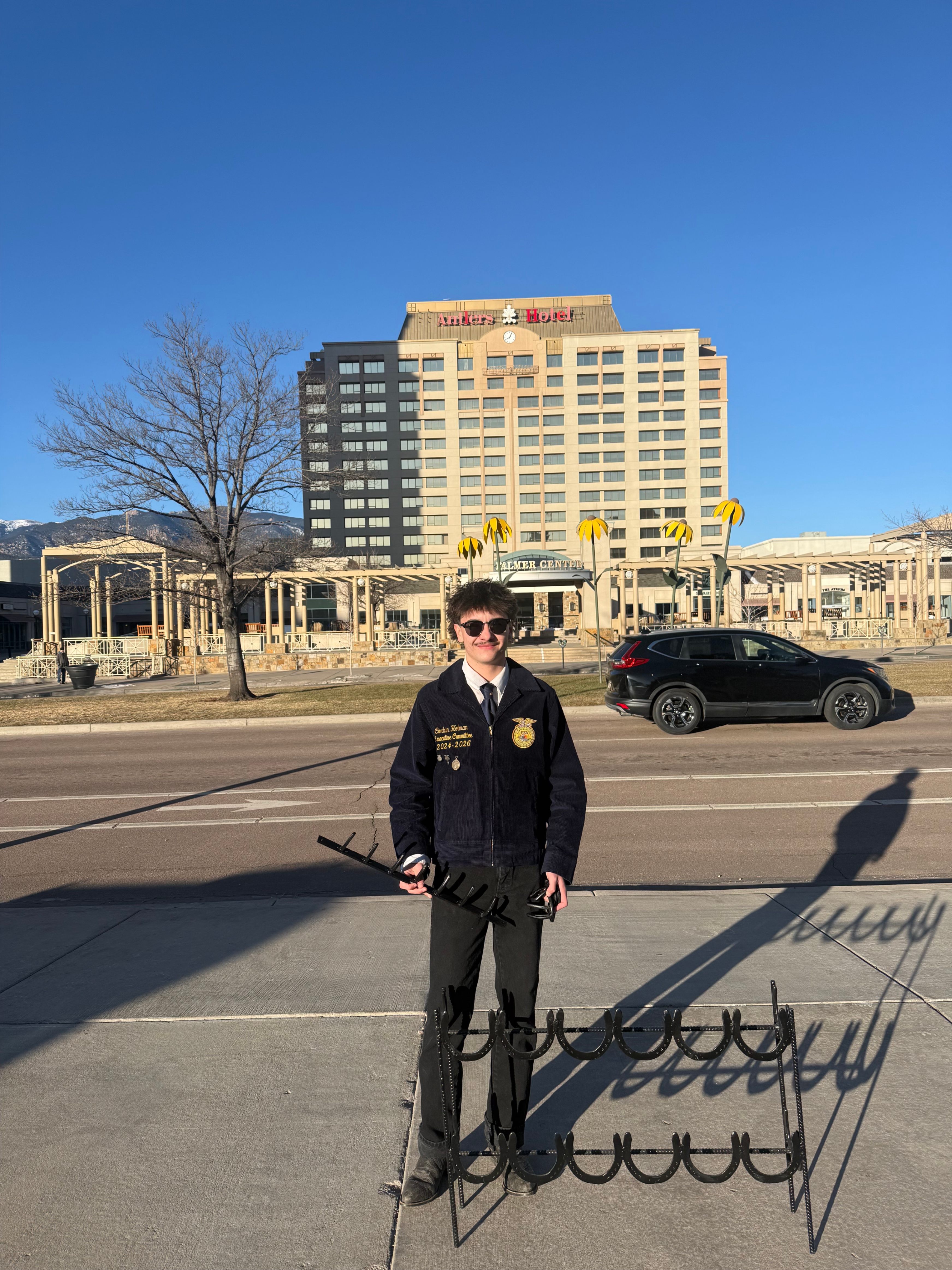 Student in a FFa jacket standing in front of a building with a horse shoe rack.