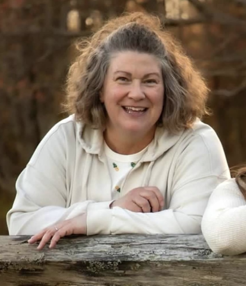 Smiling woman in white leaning on a log 