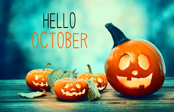 A "Hello October" image with four carved, glowing jack-o'-lanterns and fall leaves on a rustic wooden surface against a teal and green bokeh background.