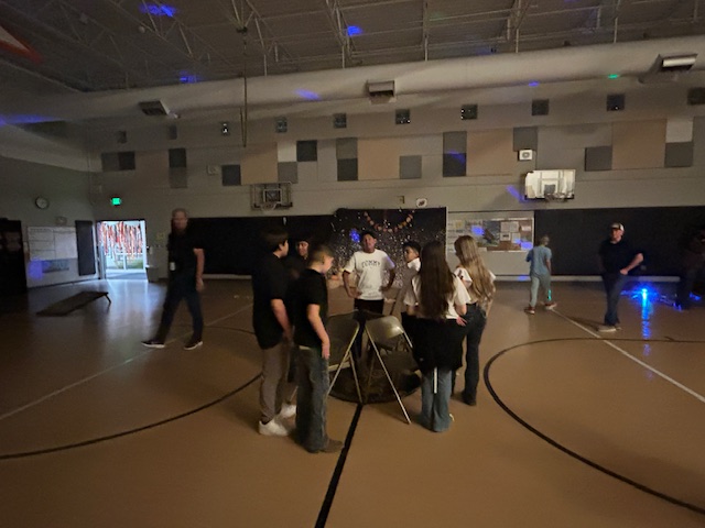 Children playing a game (musical chairs) in a gym near a fall-themed photo backdrop.