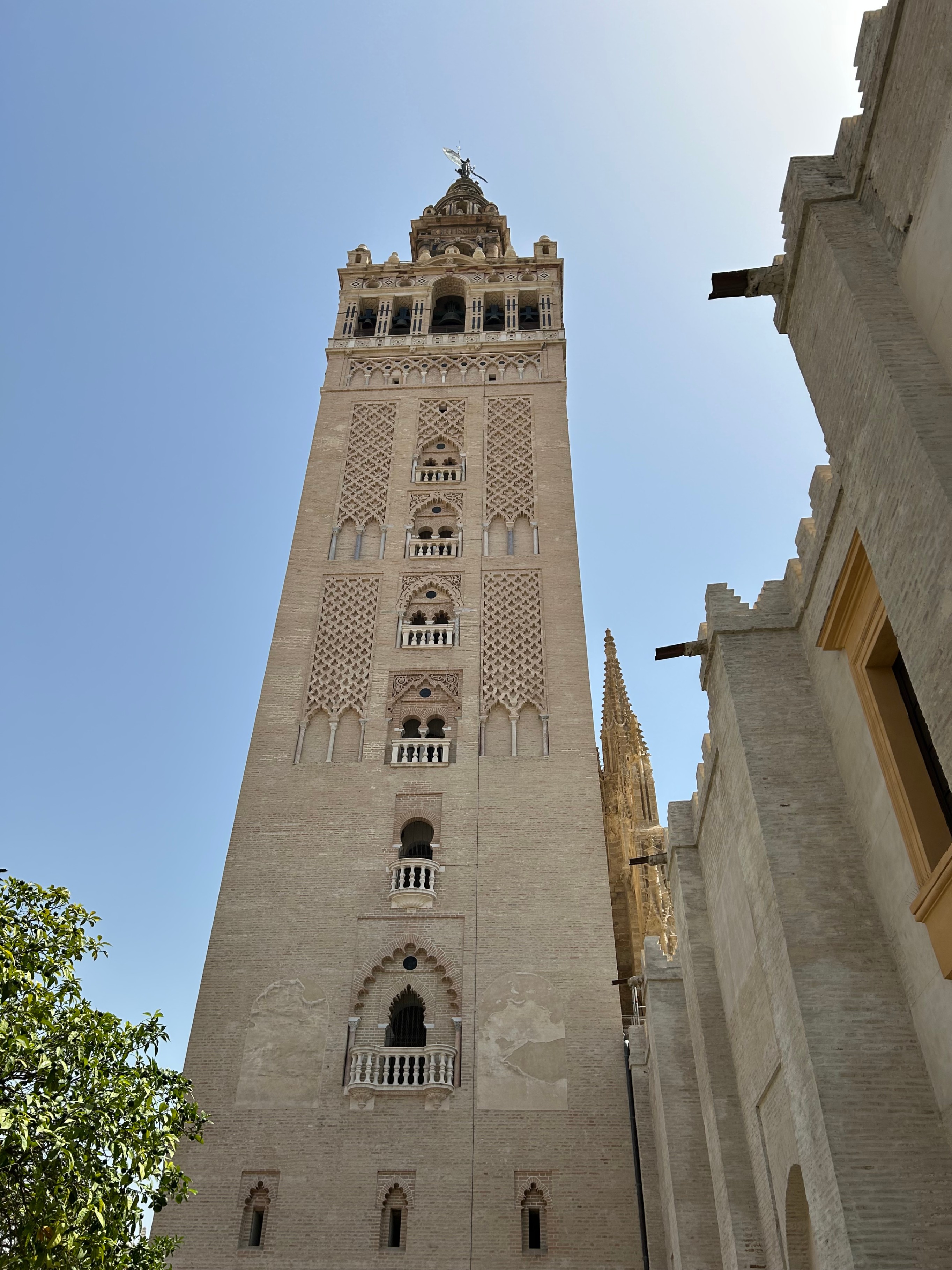 Low-angle view looking straight up at the intricate stone architecture of La Giralda bell tower against a clear blue sky in Seville, Spain.