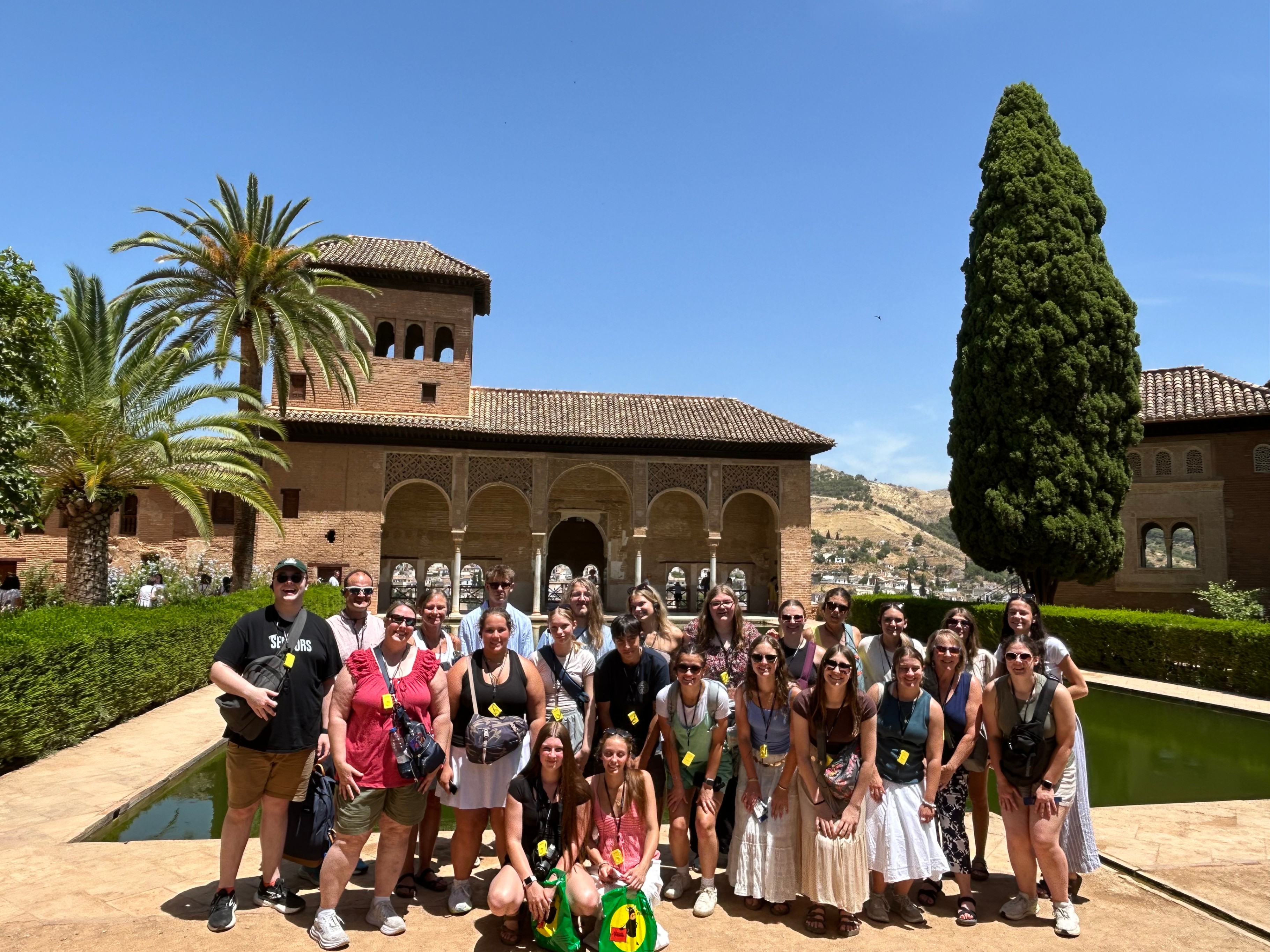 A group of students and chaperones posing in front of the historic Partal Palace and its long reflecting pool at the Alhambra.