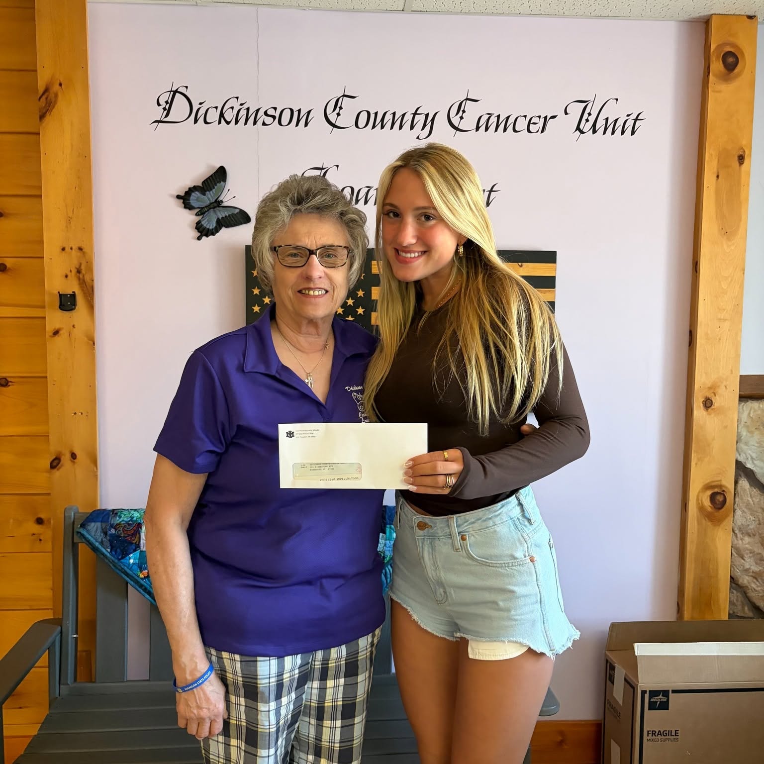 Diane Schabo from DCCC is accepting the check from Avea Brown inside the Dickinson County Cancer Unit office.