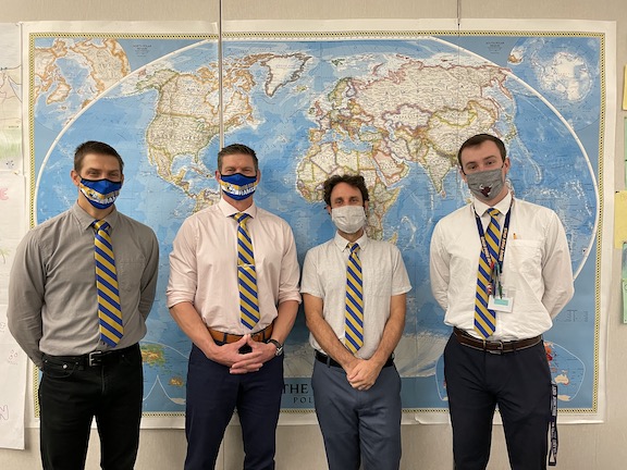 Social Studies department lined up in front of a world map all wearing matching ties