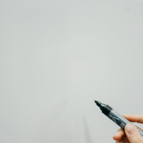 A marker held paused over the surface of a whiteboard