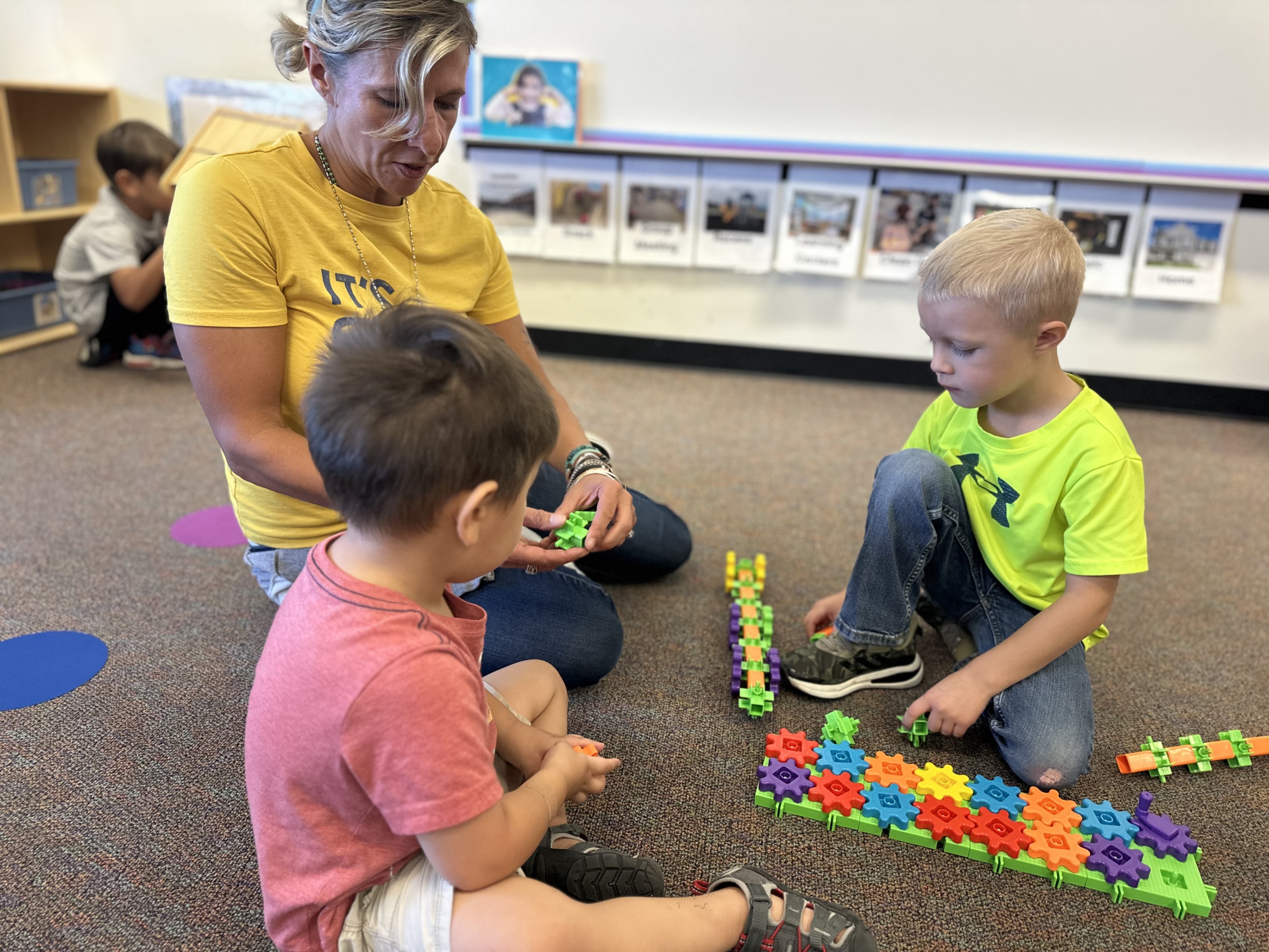 Teacher sitting on the floor playing blocks with two young male students