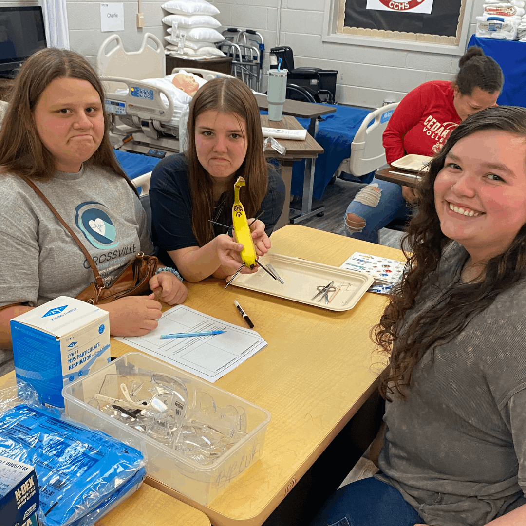 3 female students sitting at a table, one holding a banana for dissection
