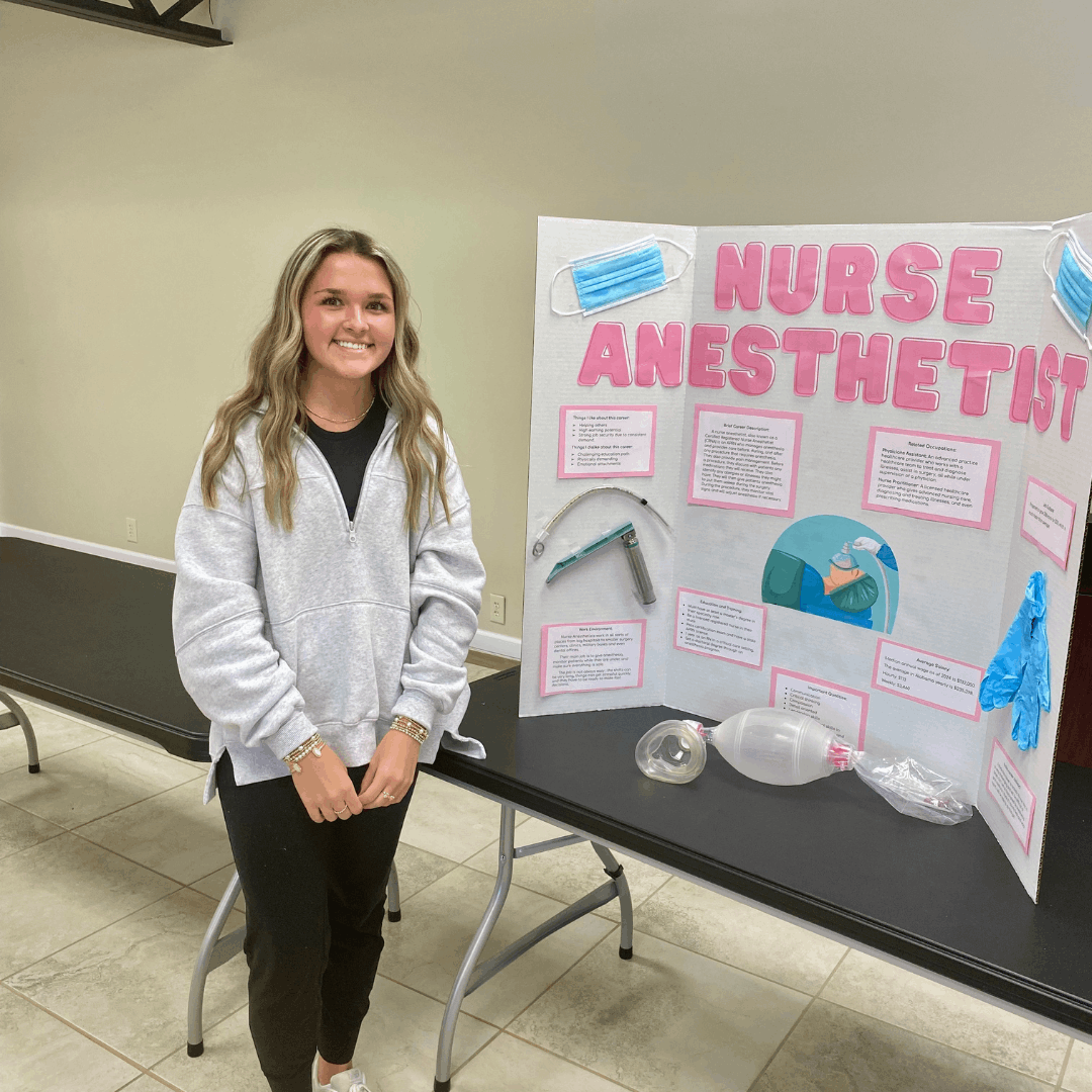 female student standing next to trifold board featuring nurse anesthestist career