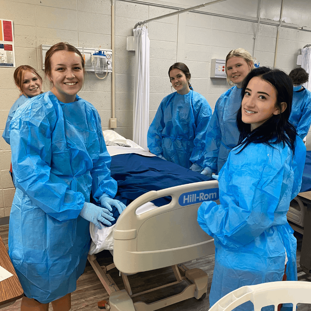 5 female students standing around a hospital bed in PPE