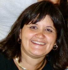 Portrait of a woman with dark hair and bangs and a big smile.