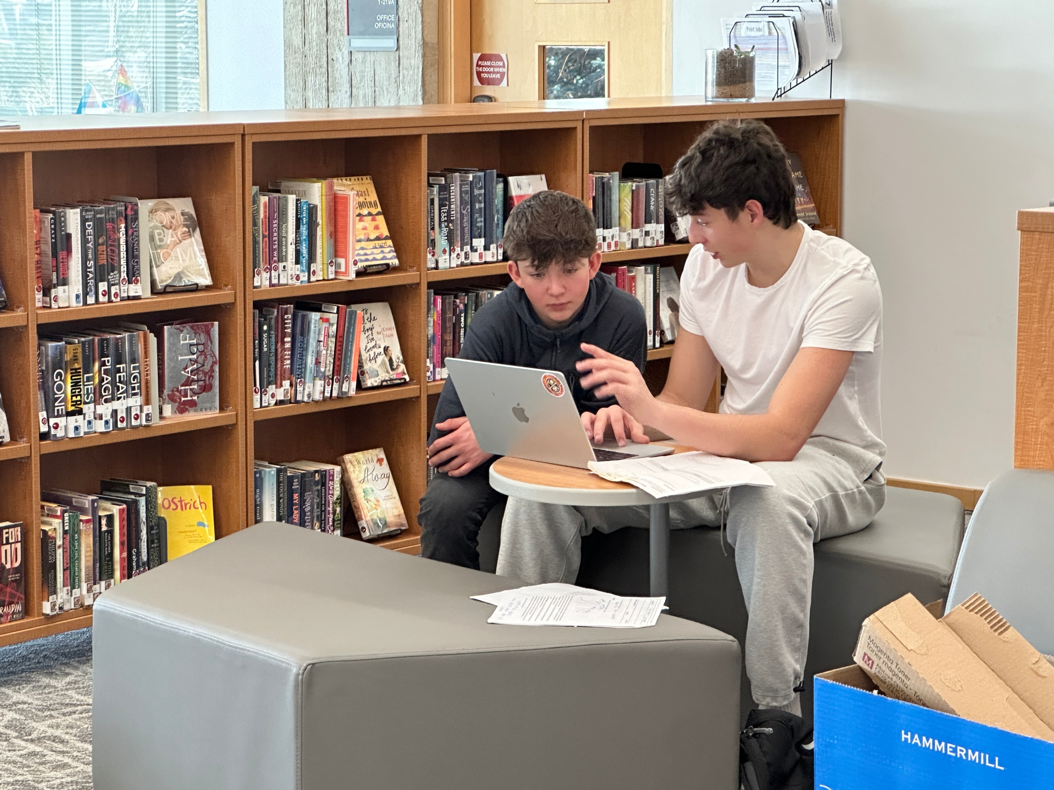 Two students collaborate on a laptop in a library.