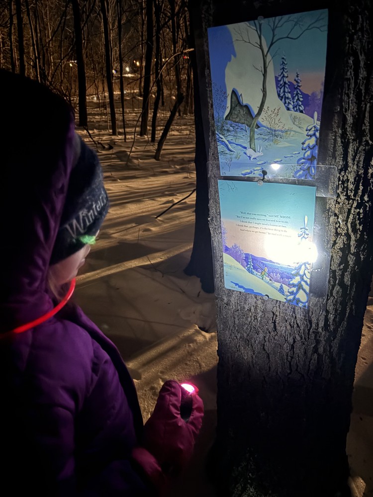 Student with a flashlight reading on a story walk